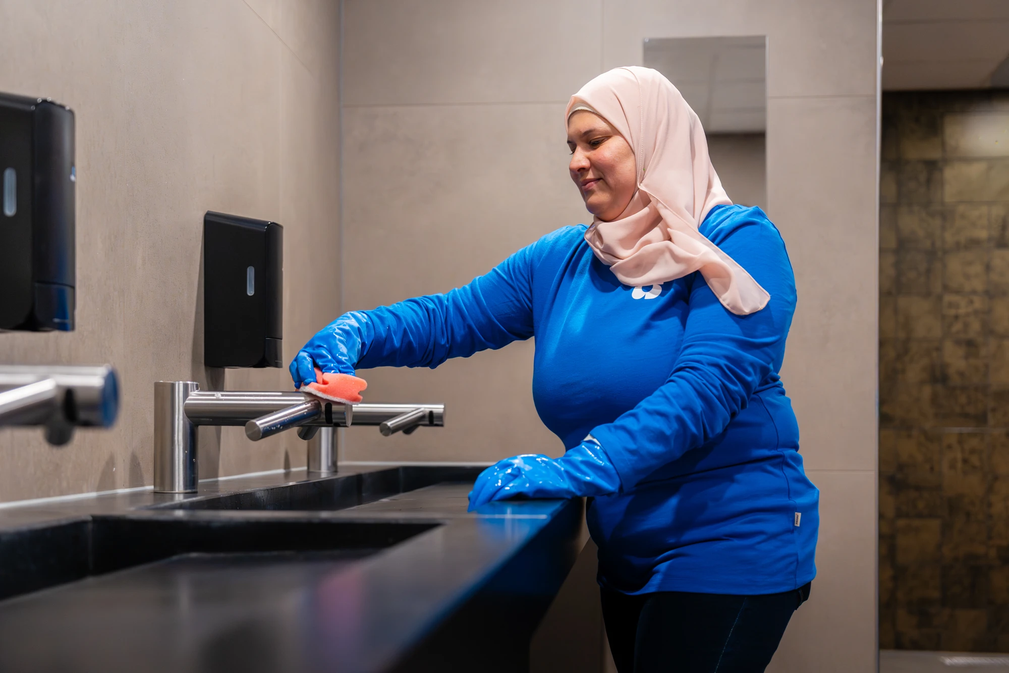 Schoonmaakster reinigt een wastafel in een sanitaire ruimte
