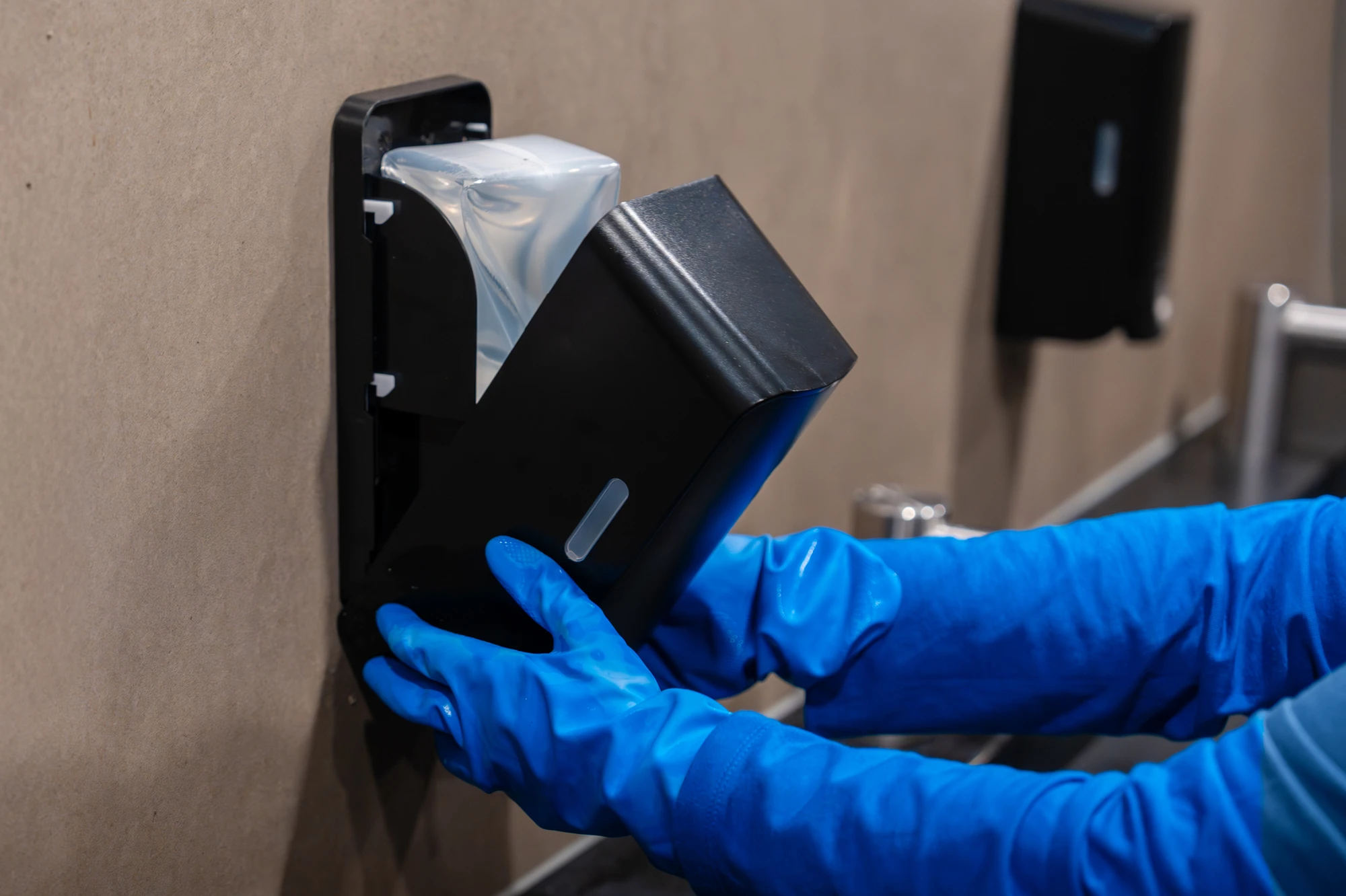 Schoonmaker reinigt een zeepdispenser in een sanitaire ruimte