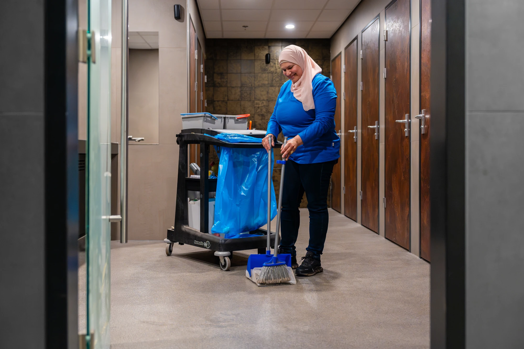 Medewerker met schoonmaakkar in een gang